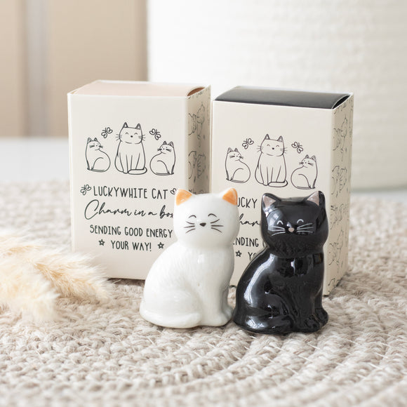 White and black cat-shaped ceramic figures with packaging on a textured surface