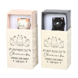 Two cat-shaped charms in boxes with text on a white background