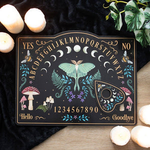 Decorative Ouija board with mystical design on a dark surface with candles and plants.