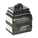 Stack of books titled 'Cat Magick', 'Lunar Wisdom', and 'Whiskers & Wonders' with a cat figurine on top.