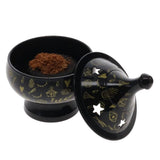 Black container with decorative lid featuring symbols, open to reveal a powdery substance inside.