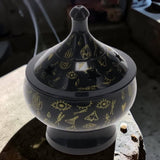 Black ceramic incense burner with gold designs on a stone surface