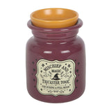 A ceramic witch-themed jar candle labeled 'Mischief and Magic Trickster Tonic' in a deep plum purple color, featuring a contrasting mustard-yellow inner cup and a vintage-style cream label with a black witch hat illustration.