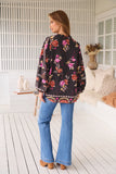 Woman wearing a floral blouse and jeans in a bright room.