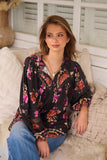Woman wearing a floral blouse sitting on a couch with a neutral background