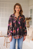 Woman wearing a black floral blouse and blue jeans in an indoor setting.