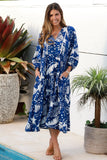 Woman wearing a blue and white patterned dress standing by a pool with plants around.