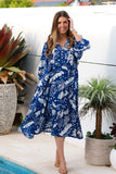 Woman in a blue and white patterned dress standing by a pool with plants around.