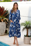 Woman in a blue patterned dress standing by a pool with plants around.