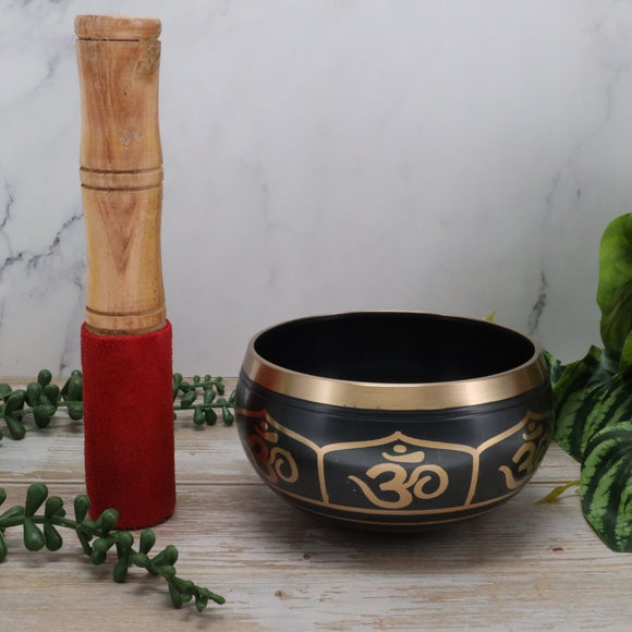 Tibetan singing bowl withOm symbol, wooden stick, and red sleeve on a marble background