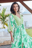 Woman in a green and white patterned dress standing outdoors with a blurred background