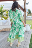 Woman in a green and white patterned dress standing on a wooden deck.