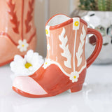 Ceramic mug shaped like a cowboy boot with floral designs on a white surface.