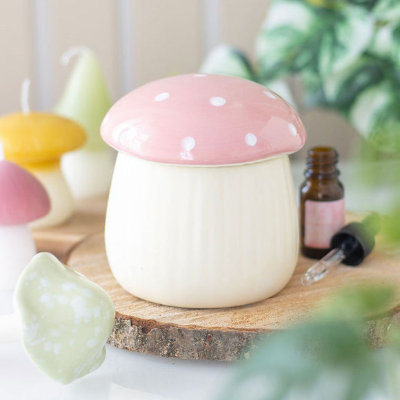 Mushroom-shaped oil burner on a wooden surface with candles and essential oils in the background