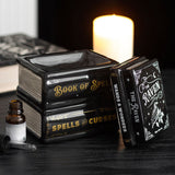 Decorative books titled 'Book of Spells', 'Spells & Curses', and 'The Raven' on a dark surface with a candle in the background.