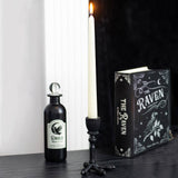 Decorative bottle, candle, and book titled 'The Raven' on a dark surface.