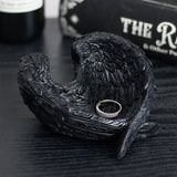 Black raven wings ring holder with a ring inside on a dark surface