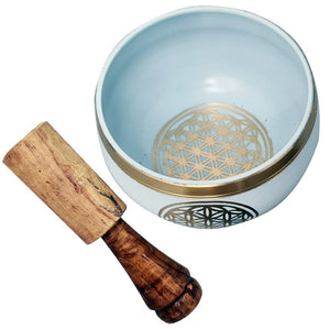 White singing bowl with gold and black designs and a wooden mallet on a white background