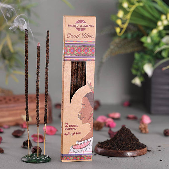 Incense sticks with packaging labeled 'Good Vibes' on a gray surface with plants in the background.