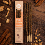 A package of Saborita Madre Palo Santo incense sticks stands upright on a dark wooden surface beside several incense sticks. The box is kraft paper with peach-colored panels and reads 'Saborita Madre' and 'Palo Santo Sustainable.