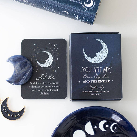 Sodalite crystal, packaging, and decorative items with celestial design on a white surface