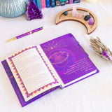 Purple notebook with celestial design on a white surface with mystical items.