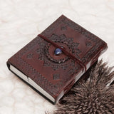 Brown leather journal with decorative embossing and string closure on a textured surface.