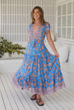 Woman wearing a blue floral dress on a white wooden deck.