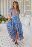 Woman wearing a blue floral dress standing on a wooden deck.