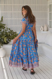 Woman wearing a blue floral dress standing on a wooden deck.