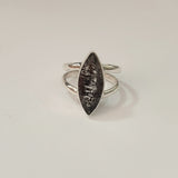 Silver ring with a textured black stone on a light gray background
