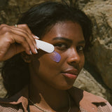 Woman applying sunscreen to her face with a spatula against a rocky background