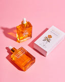 Two orange glass bottles with droppers and a white box on a pink background