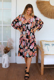 Woman wearing a floral dress standing in a room with a white door and decorative items.