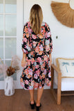 Woman wearing a floral dress in a room with a chair and decorative items.
