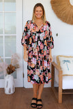 Woman wearing a floral dress standing in a room with a white door and decorative items.