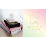 Stack of books with a crystal on a white surface, next to a colorful cover with text and symbols.