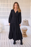 Woman wearing a black dress standing in a modern indoor setting with white walls and wooden floor.