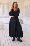 Woman wearing a black dress standing on a wooden deck with white railing and cushions.