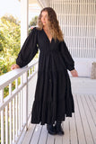 Woman in a black dress standing on a balcony with white railings and greenery.