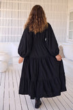Person wearing a black dress standing on a wooden deck with white railing.