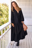 Woman in a black dress standing on a wooden deck with greenery in the background