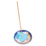 Incense holder with a blue design featuring a face and nature elements on a white background.