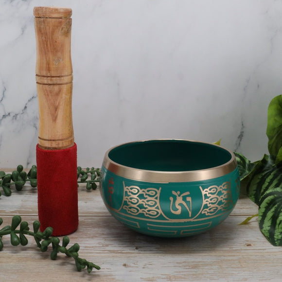 Green singing bowl with gold patterns and a wooden mallet on a light background