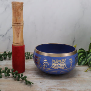 Blue singing bowl with gold designs and wooden mallet on a marble surface