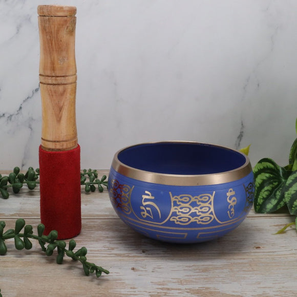 Blue singing bowl with gold designs and wooden mallet on a marble surface