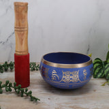 Blue singing bowl with gold designs and wooden mallet on a marble surface