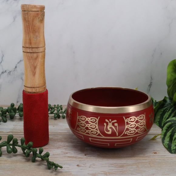 Red singing bowl with gold patterns and a wooden mallet on a marble surface.