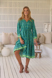 Woman wearing a green patterned dress in a bright room with white walls and wooden floor.