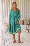 Woman wearing a green patterned dress standing on a wooden deck.